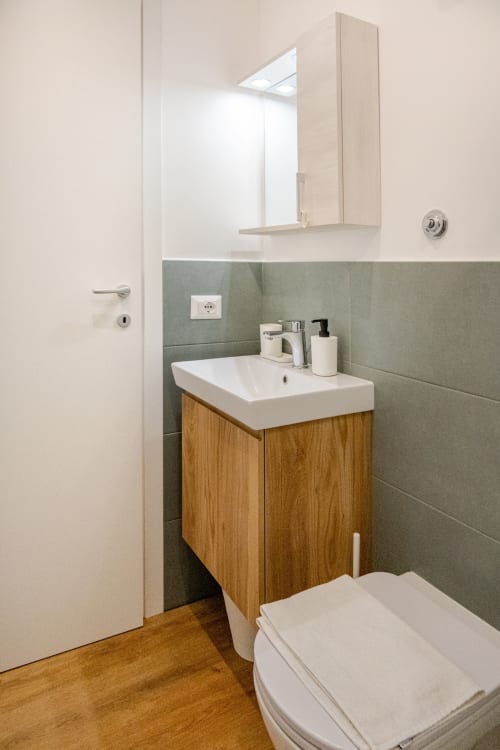 Bagno moderno nell'appartamento Art House Roma con mobile in legno, lavabo bianco, specchiera e piastrelle verdi