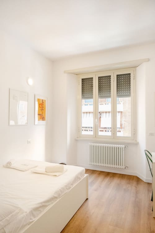 Camera luminosa e minimalista nell'appartamento Art House Rome con letto bianco, pavimenti in legno, radiatore e finestre a triplo vetro