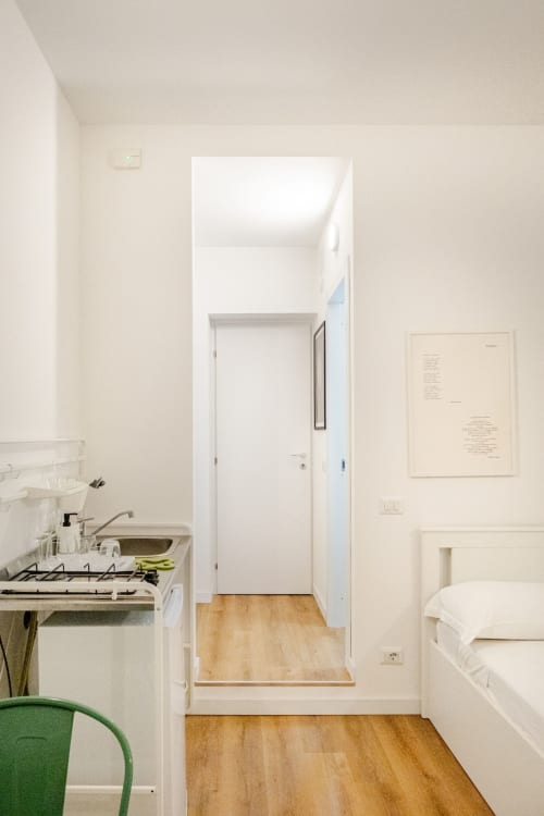 Cucina compatta in appartamento romano con fornello, pareti bianche, pavimento in legno e porta aperta verso la camera da letto presso Art House