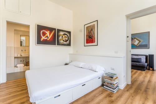 Camera da letto moderna presso Art House Rome con letto bianco, bagno en suite, quadri incorniciati, pavimenti in legno e zona living adiacente
