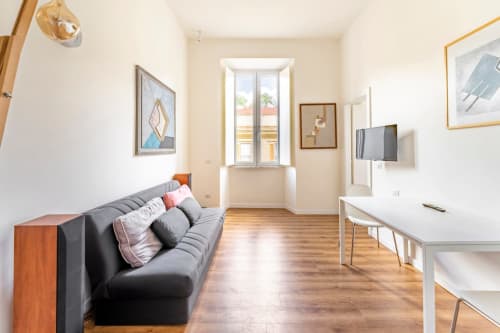 Moderno appartamento in Piazza del Popolo a Roma con divano nero, pavimenti in legno, TV e luminosa finestra con vista sulla strada.