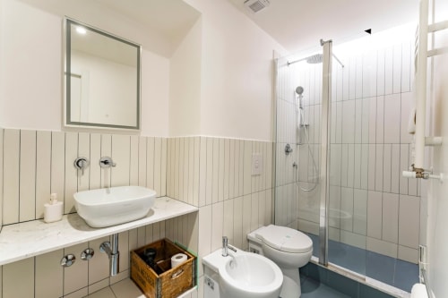 Bagno moderno ad Art House Rome con lavabo a bacinella, bidet, box doccia e pareti rivestite in piastrelle verticali