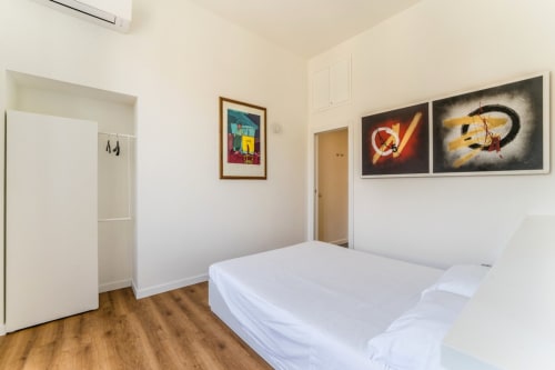 Camera moderna presso Art House Rome con letto bianco, pavimento in legno, opere d'arte colorate e servizi come aria condizionata e Wi-Fi