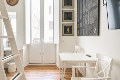 Luminoso appartamento moderno a Roma con tavolo da pranzo bianco, sedie, pavimenti in legno e porte-finestre con vista sulla città.