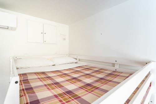 Letto bianco con biancheria scozzese nell'appartamento Art House di Roma, con arredi essenziali e pareti bianche