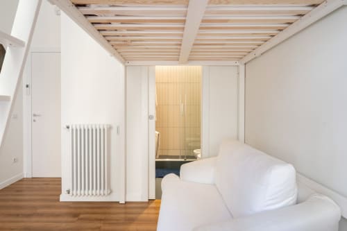 Camera da letto minimalista e luminosa nella casa di lusso Art House Rome con travi in legno, biancheria bianca, radiatore e dettagli in legno