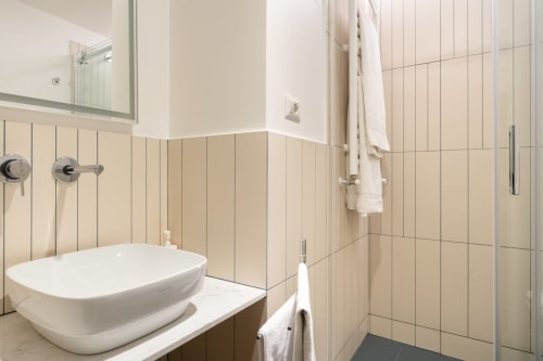 Bagno moderno dell'appartamento Art House Rome con lavabo in ceramica bianca, rivestimenti in piastrelle beige, soffione pioggia e asciugamani bianchi