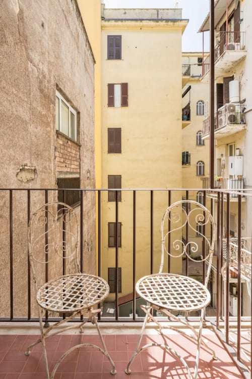 Due eleganti sedie bianche su un balcone in terracotta con vista sui storici edifici gialli di Roma, presso l'Art House apartment hotel.