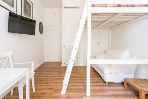 Moderno loft ad Art House Roma con letto rialzato, arredamento bianco, pavimento in legno e TV in camera da letto.