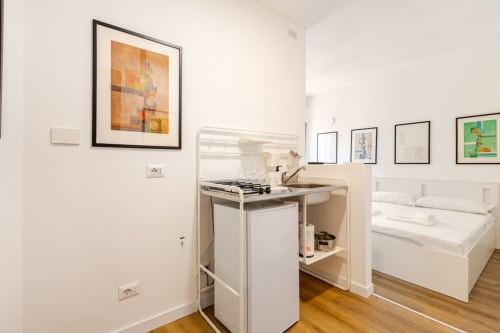 Moderno monolocale a Roma con angolo cottura, lavatrice, letto matrimoniale e opere d'arte contemporanea su pareti bianche.