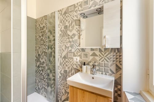 Bagno moderno ad Art House Roma con piastrelle geometriche decorate, lavabo bianco, mobile in legno e box doccia in vetro