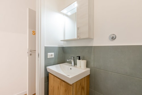 Moderno bagno dell'Art House Rome con lavabo bianco, vanity in legno, piastrelle grigie, specchio a parete e finiture cromate