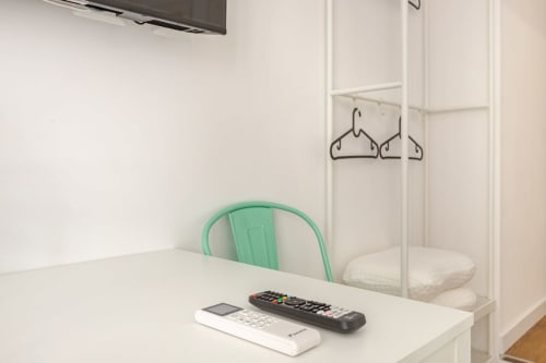 Spazio di lavoro in appartamento Art House Roma con sedia verde, scrivania bianca, telecomando TV, climatizzatore e armadio con appendiabiti