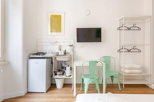 Accogliente monolocale a Roma con angolo cottura, sedie color menta, TV, scaffali bianchi e pavimenti in legno