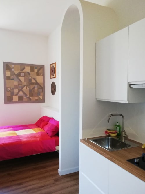Cucina e camera da letto dell'appartamento Art House Roma con biancheria rosa, lavandino e armadietti bianchi
