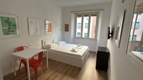 Monolocale moderno presso Art House Roma con letto, scrivania, sedie rosse, pavimenti in legno e viste sulla città