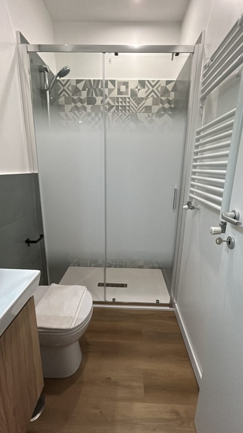 Bagno moderno nell'aparthotel Art House Rome con box doccia in vetro, wc bianco, scaldasalviette e pavimentazione in legno