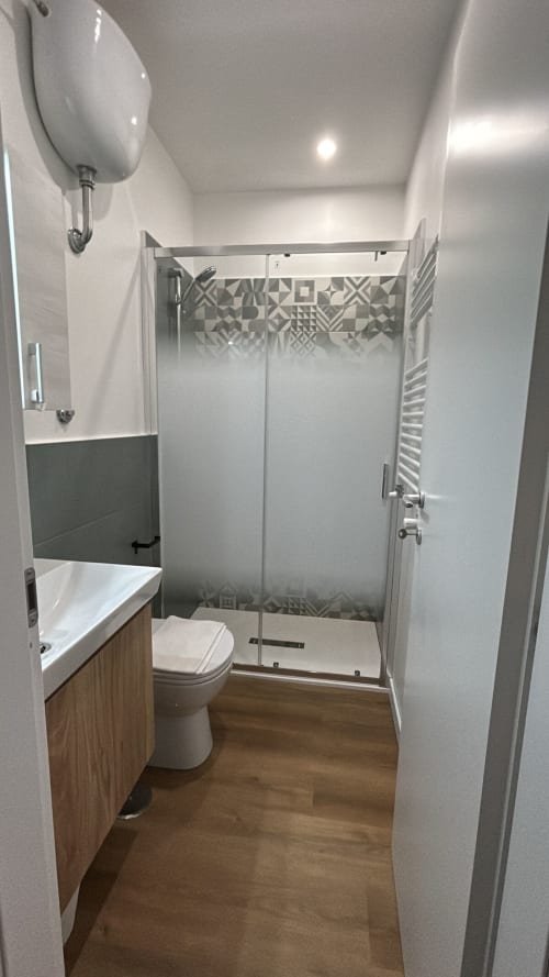 Bagno moderno nella villa Torlonia di Art House Roma con pareti bianche, mobile vanità in legno, cabina doccia in vetro e