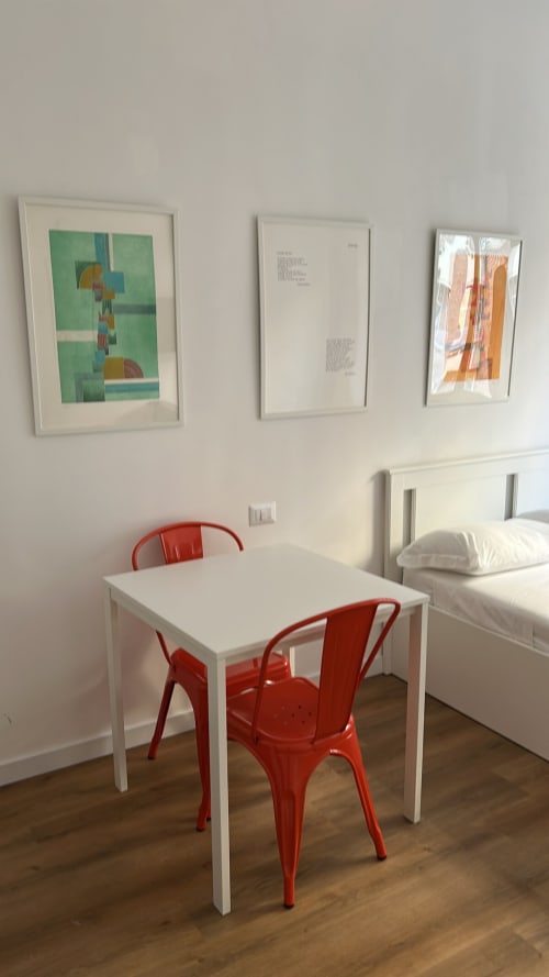 Studio moderno all'Art House Roma con scrivania bianca, sedie rosse, quadri incorniciati e letto con cuscini bianchi