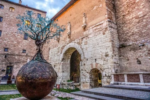 Antico cortile della Residenza San Jacopo a Spello con scultura bronzea di albero e arcata in pietra
