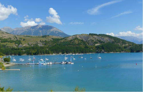 Lac alpin turquoise avec voiliers, pics montagneux et rives boisées près de Colombes
