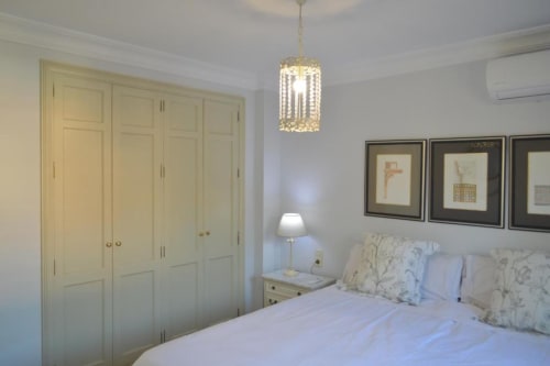 Elegante habitación en CTH Granada con armario crema, lámpara colgante, cuadros enmarcados y cama con almohadas decorativas