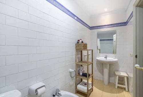 Baño moderno con azulejos blancos tipo metro, lavabo pedestal, espejo, estantería de almacenamiento de madera y cenefa decorativa azul en CTH