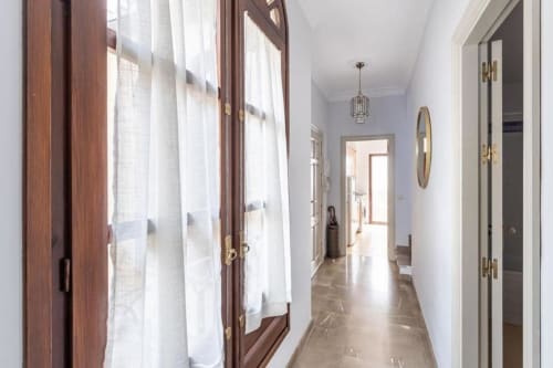 Pasillo luminoso con puertas de madera, paredes blancas, lámpara colgante y suelos de mármol en el apartamento CTH Granada de Armilla