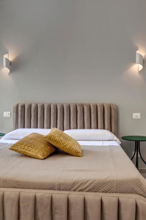Modern bedroom at Palazzo Belvedere with pleated headboard, yellow pillows, and wall sconces