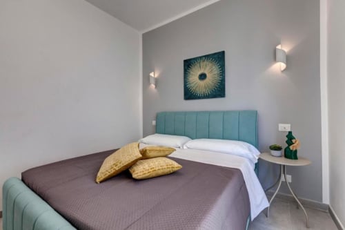 Modern double bedroom at Palazzo Belvedere with teal headboard, white bedding, gold pillows, and contemporary sunburst
