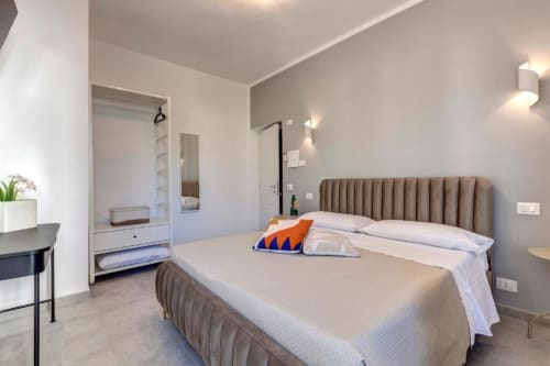 Modern double bedroom at Palazzo Belvedere with taupe headboard, white linens, desk area, and en-suite bathroom entrance