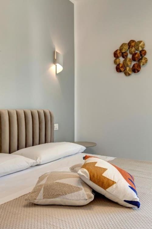 Modern double bedroom at Palazzo Belvedere with beige headboard, decorative pillows, wall sconces, and gold wall art