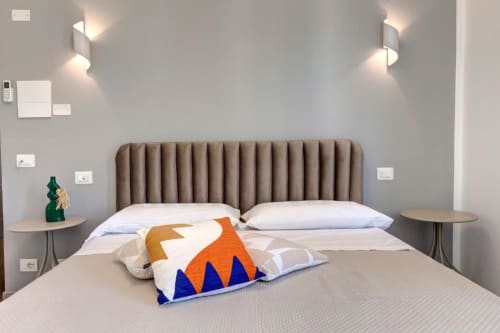 Modern double bedroom at Palazzo Belvedere hotel with taupe headboard, white bedding, colorful pillow, wall sconces, and side