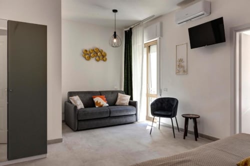 Modern suite living area at Palazzo Belvedere with gray sofa, dark chair, pendant light, wall art, and flat-screen TV