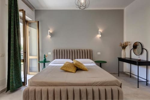 Modern bedroom suite at Palazzo Belvedere with gray upholstered bed, yellow pillows, green curtains, and landmark views from