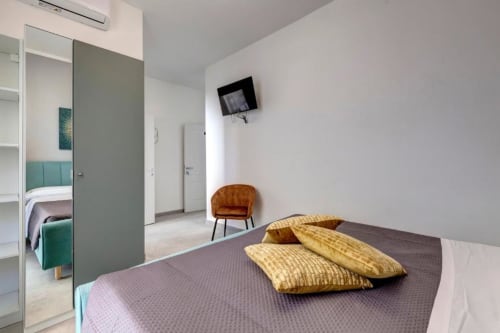 Modern double bedroom at Palazzo Belvedere with twin beds, green accents, mirror, TV, and contemporary furnishings in
