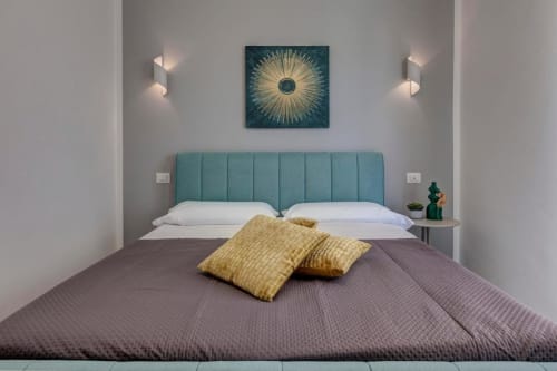 Modern bedroom at Palazzo Belvedere Chianciano Terme with turquoise headboard, gold pillows, and contemporary sun artwork