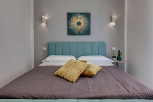 Modern double bedroom at Palazzo Belvedere with teal headboard, white pillows, gray bedding, and gold cushions in Chianciano
