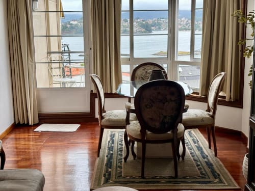 Elegante comedor del apartamento de Baiona con vistas al mar, suelos de madera y sillas clásicas con vista a las aguas de la bahía