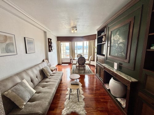 Elegante sala de estar en apartamento de Baiona con vistas al mar, sofá beige, pisos de madera y centro de entretenimiento