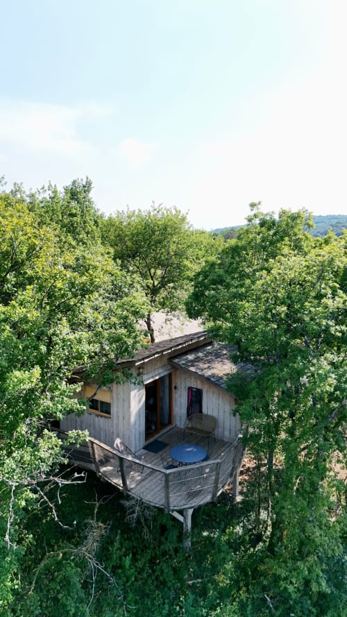 Treehouse cabin nestled in lush green trees with deck and mountain views at Cabanes et lodges du Belvédère, Serrières-sur-Ain