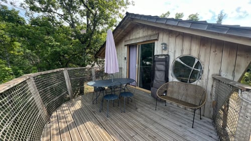 Terrazza in legno della villa La Chenaie con tavolo da pranzo, sedie, ombrellone e area lounge con vista sul fiume