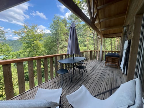 Ampio terrazzo in legno del Lodge Le Taillet con tavolo da pranzo esterno, sedie, ombrellone e zona relax affacciata sul verde