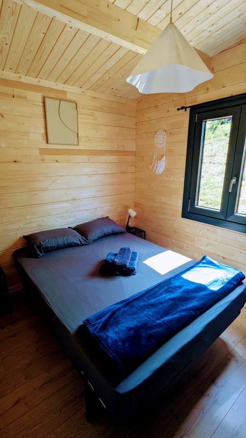 Accogliente camera da letto in lodge in legno con letto queen, biancheria blu, lampada a sospensione e porta-finestra nera