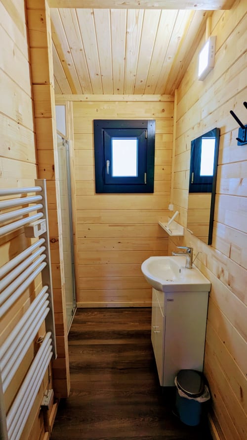 Bagno moderno in legno con lavabo bianco, scaldasalviette e finestre con cornice nera presso il lodge LA BRUYERE di Cabanes et lodges