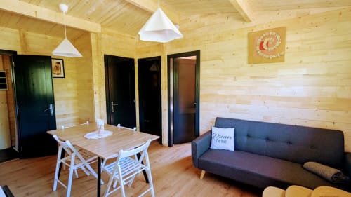 Interno moderno di lodge in legno con tavolo da pranzo, divano grigio e lampade a sospensione presso Cabanes et lodges du Belvédère