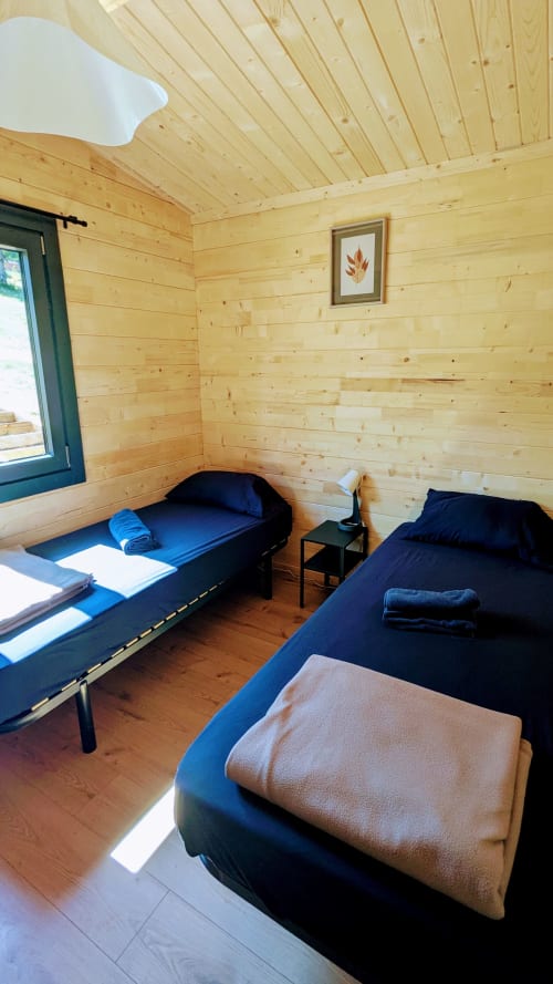 Accogliente camera da letto in lodge di legno con due letti, biancheria blu e vista sul fiume alle Cabanes du Belvédère a Serrières-sur-Ain
