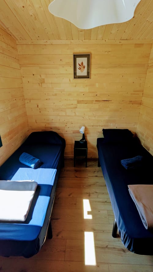 Accogliente camera da letto in legno con due letti, biancheria blu e stampe di foglie incorniciate presso Cabanes et lodges du Belvédère