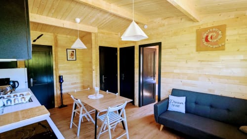 Interno moderno di lodge in legno con tavolo da pranzo, cucina e divano scuro presso Cabanes du Belvédère, Serrières-sur-Ain