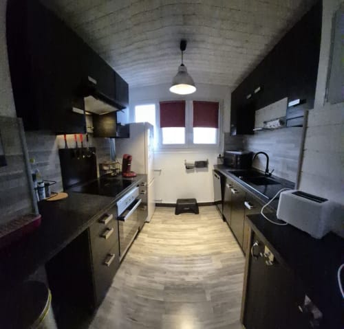 Cuisine couloir moderne de l'appartement Val'Déco aux Ponts de Cé, avec meubles noirs, électroménagers inox et bois